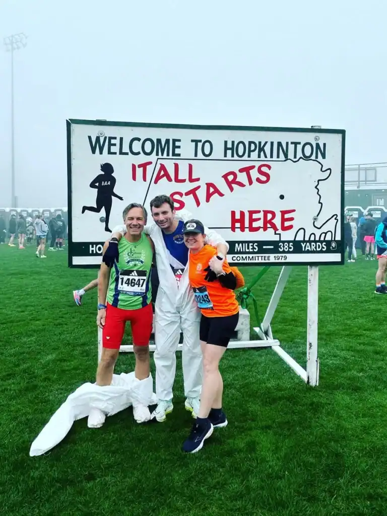 Three runners posing at Hopkinton race start sign