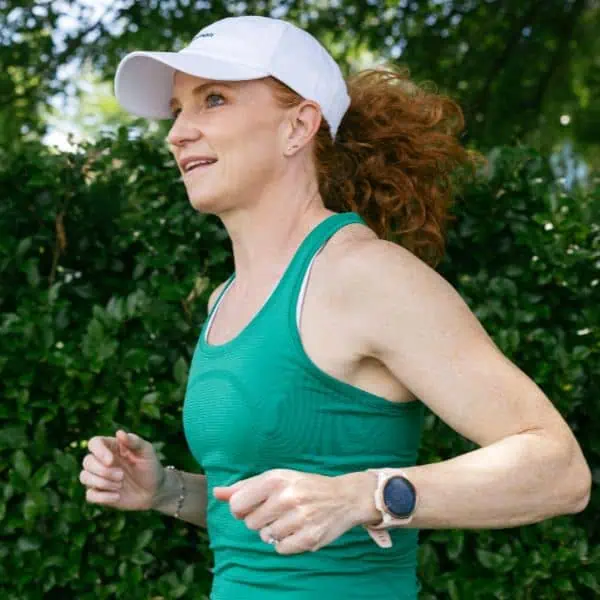 Woman jogging outdoors wearing white cap and smartwatch